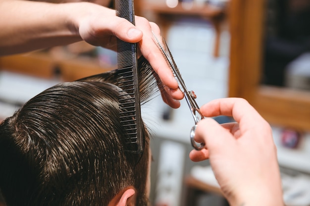 Closeup of barbers hands making short haircut to man using comb and scissors in barbershop