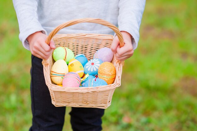 Canestro del primo piano con le uova di pasqua variopinte in mani dei bambini