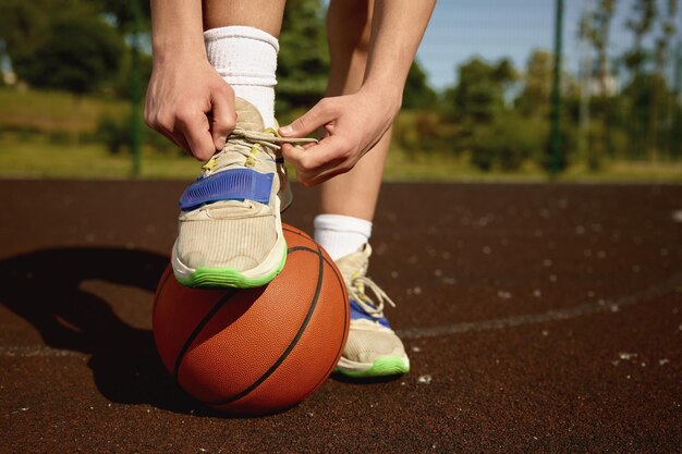 Closeup basketball player tying laces on training sneakers putting foot on ball