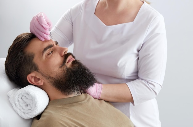 Closeup of bearded man getting beauty injection at aesthetic clinic Doctor injecting antiaging filler in handsome male face