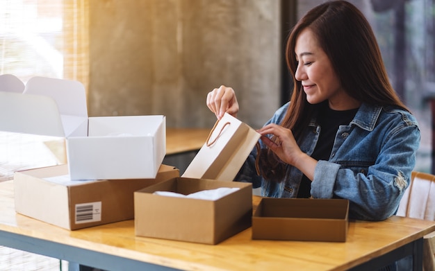 Primo piano di bella donna asiatica che si apre e che guarda il sacchetto della spesa interno a casa per la consegna e il concetto online di acquisto