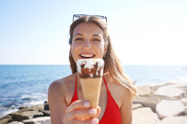 Крупный план красивой женщины в бикини, держащей рожок мороженого, итальянское мороженое, смотрящей в камеру на пляже летом