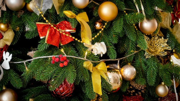 Closeup beautiful Christmas tree decorated with golden and red baubles and garlands. Winter holidays background or backdrop.