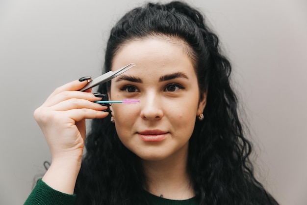 Closeup of a beautiful girl holding an eyebrow tweezer in her hand near her face in the studio