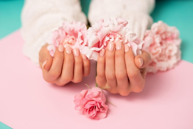 Closeup beautiful pink flowers on women's hands with manicure on nails on colored background