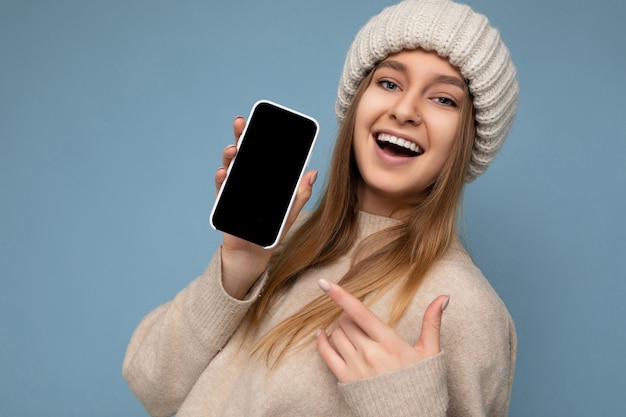 Closeup of beautiful positive young woman wearing stylish beige sweater and beige knitted winter hat