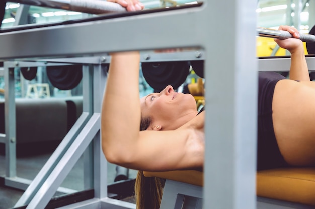 Primo piano di una bella donna che fa esercizi con bilanciere su una panca che si allena in un centro fitness