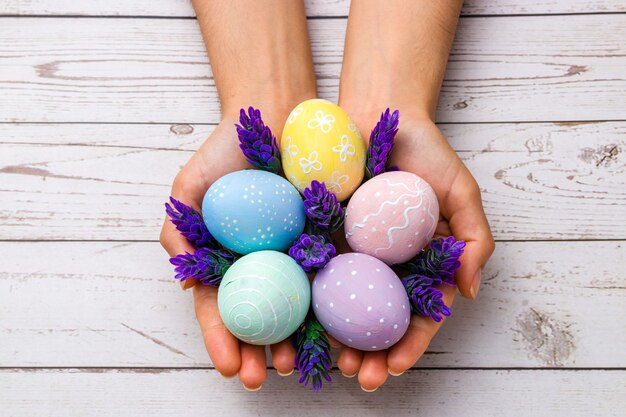 closeup beautiful woman hands holding hand-painted easter eggs in tender pastel colors and lavender flowers over wooden table