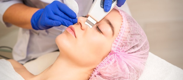 Photo closeup of beautiful young woman receiving ultrasound facial exfoliation and cavitation facial peeli...