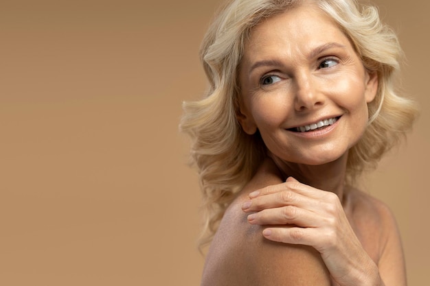 Closeup beauty portrait of smiling mature woman looking aside at copy ad space on beige background