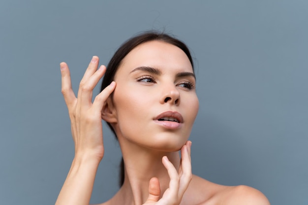 Closeup beauty portrait of a topless woman with perfect skin and natural makeup on light blue wall background