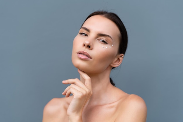 Closeup beauty portrait of a topless woman with perfect skin and natural makeup with antiaging cream dots to moisturize and firm the skin under the eyesx9