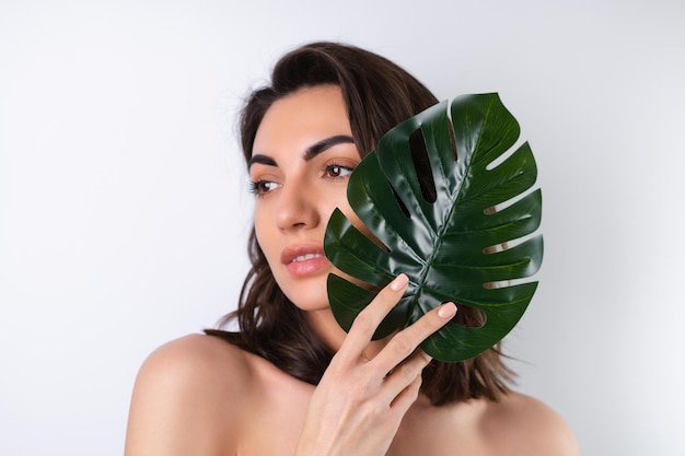 Closeup beauty portrait of a topless woman with perfect skin and natural makeup with monstera palm leaf