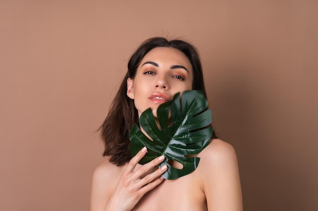 Photo closeup beauty portrait of a topless woman with perfect skin and natural makeup with monstera palm leaf