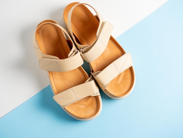 Closeup of beige leather sandals on a white and blue background A pair of shoes womens summer shoes top view flat lay