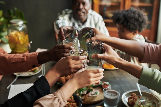 Closeup of big family holding glasses with lemonade and toasting together while having holiday dinner at table