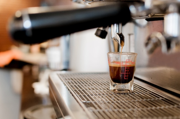 Il caffè nero del primo piano nella tazza di misurazione ha messo sulla caffettiera, macchina per il caffè che fa l'espresso