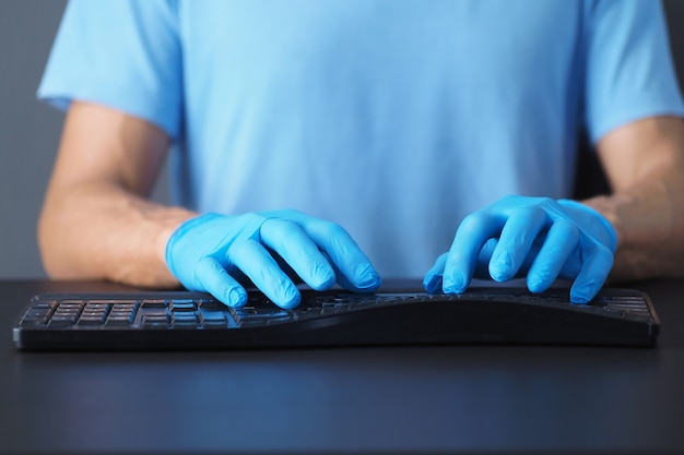 Foto primo piano della tastiera e delle mani di computer nere in guanti blu del lattice.