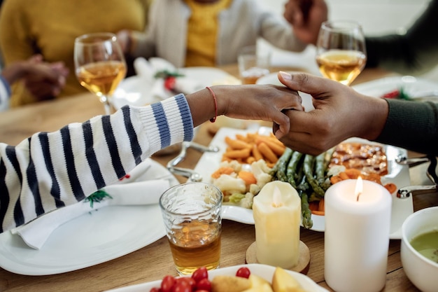 Closeup of black family praying during Christmas lunch at dining table