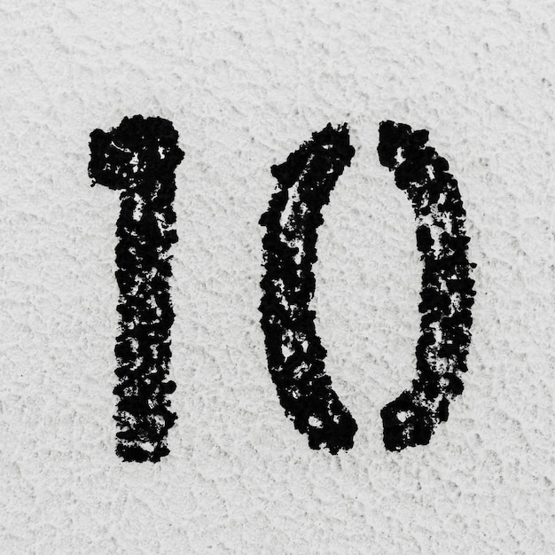 Photo closeup of black painted number of 10 on background of grey textured wall