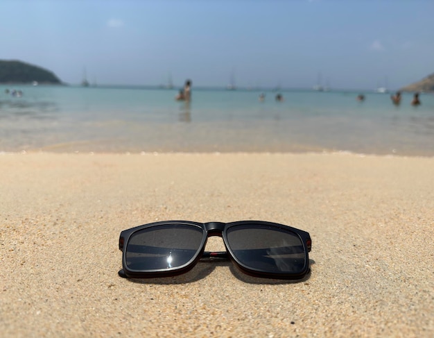 Closeup of black protective sunglasses on sandy beach at tropical seaside on warm sunny day