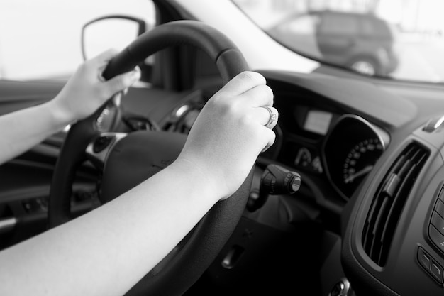 Closeup black and white image of woman holding car steering wheel