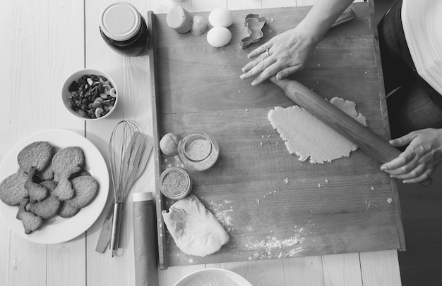 Photo closeup black and white photo of woman making dough for holiday cookies on wooden desk