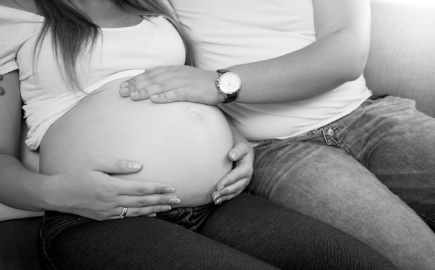 Closeup black and white photo of young man holding hand on pregnant wife tummy