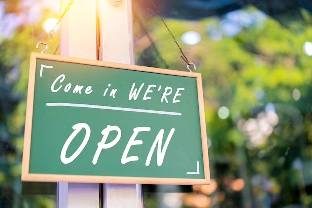 Closeup blackboard sign hanging at the shop door is labeled Come in We're OPEN The business is open for normal service