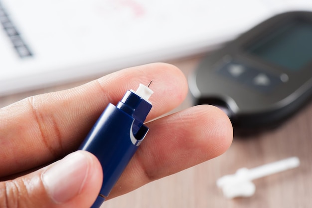 Closeup blood lancet device, used for blood testing. Blood glucose meter for diabetics in background.