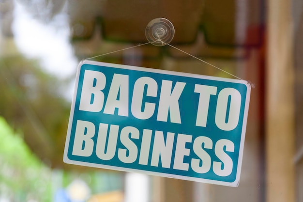 Closeup on a blue closed sign in the window of a shop
displaying the message back to business