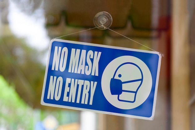 Closeup on a blue closed sign in the window of a shop displaying the message No mask no entry