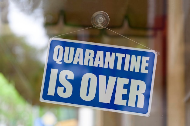 Closeup on a blue closed sign in the window of a shop displaying the message Quarantine is over