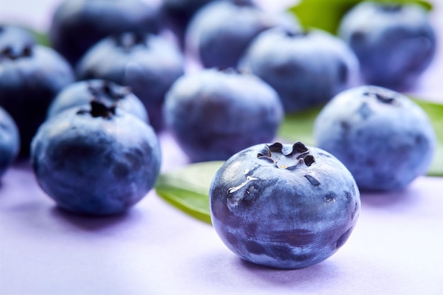 Closeup of a blueberry with green leaves and water drops on a purple background