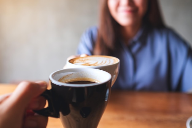 Closeup blurred image of a woman and a man clinking coffee mugs together in cafe