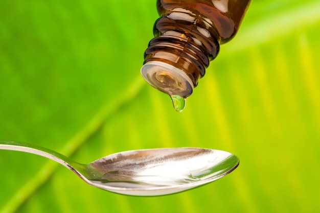 Closeup of a bottle pouring drops on a spoon with leaf on background