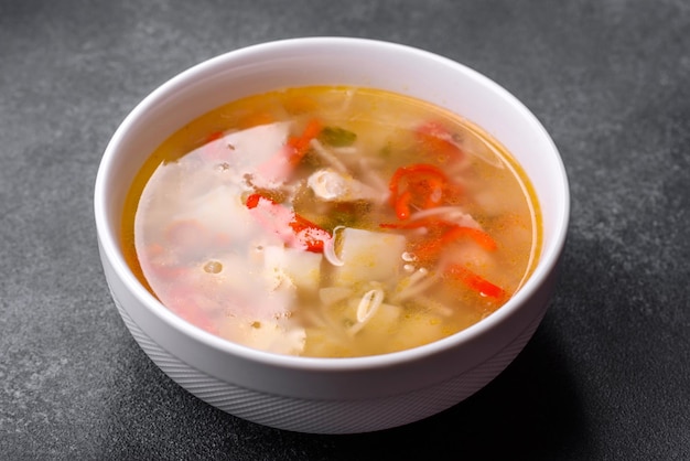 Closeup of a bowl of chicken noodle and vegetable soup on a concrete table