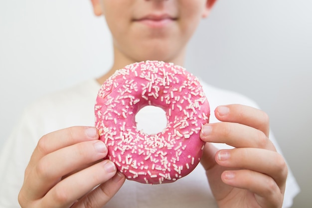 ピンクのアイスで美味しいドーナツを食べている男の子のクローズアップ写真 口がドーナツを食べている