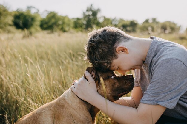 Photo closeup of a boy hugging a pit bull dog close touching foreheads