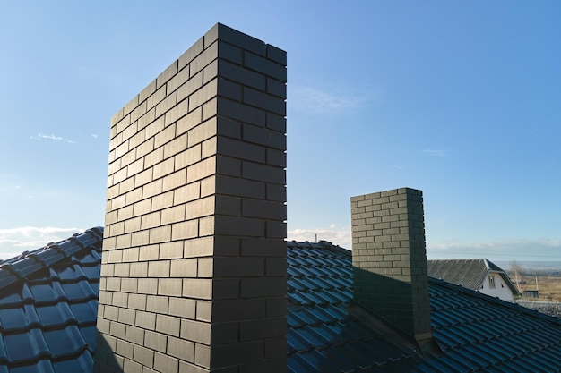 Closeup of brick chimney on house roof top covered with ceramic shingles. Tiled covering of building