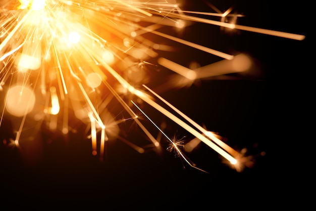 Closeup of a bright orange fire from a burning sparkler burns in the dark