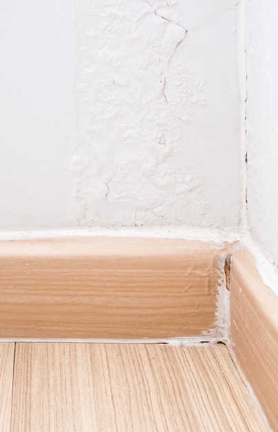 Closeup of the broken flooring skirts at the corner of the
living room, the paint on the wall has peeled off due to moisture
from the rain. front view with the copy space.