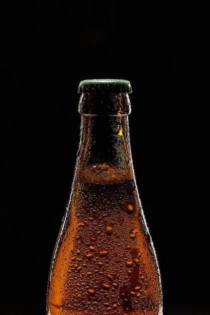 Closeup of brown beer bottle with green cap against black background bubbles lager foamy beer