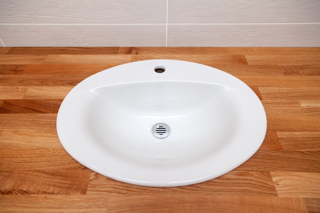 Photo closeup brown teak wooden empty tabletop with white round ceramic sink.  repair, bathroom renovation in apartments, hotel, spa, installation plumbing, faucet