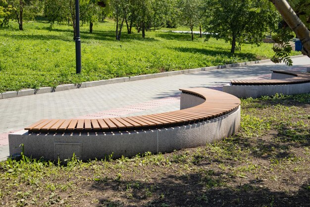 Foto close-up di una panchina di legno marrone a forma di arco in un parco della città estiva