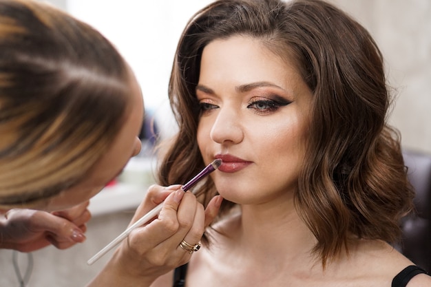 Closeup brunette young lady get ready for the event by makeup artist