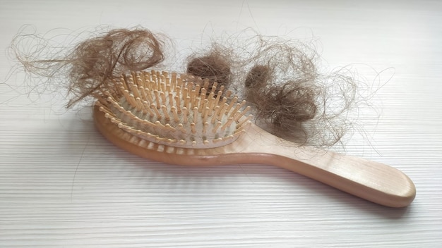 Foto primo piano di una spazzola con capelli persi su di esso su un tavolo di legno bianco