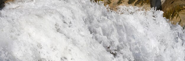 Closeup of bubbling river waterfall stream with white foam flows over stones natural wallpaper