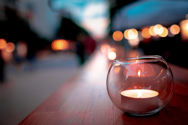 Closeup of a burning candle in a small glass jar on a wooden plank outdoors