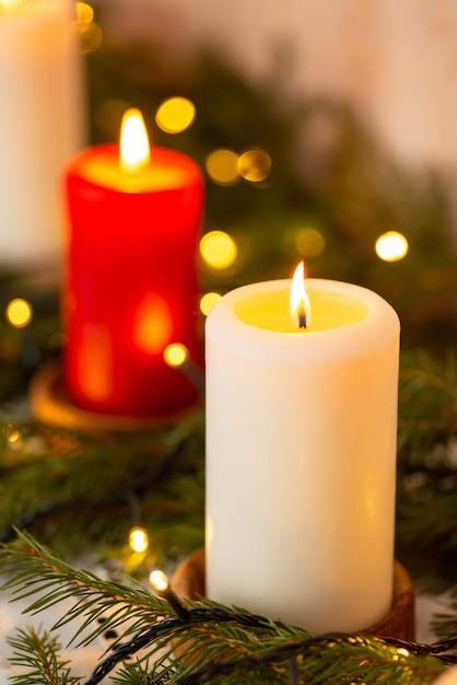 Closeup of burning candles with lights and firtree branches on top on table Christmas decorations